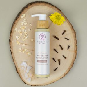 Scentral Zone Magnesium Body Lotion flat lay on wood with oatmeal, arnica flower, magnesium flakes, and clove surrounding it